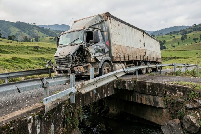 Semirreboque de carreta sobre ponte de rodovia com defensa danificada, em área rural